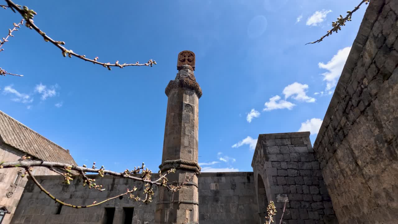 At a historic site in Cusco Peru, a stone tower stands tall against a clear blue sky. Branches of a blooming tree frame the view, showing the beauty of nature in this ancient location