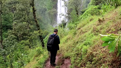 young backpacker man checking the flight of a drone in materuni waterfall