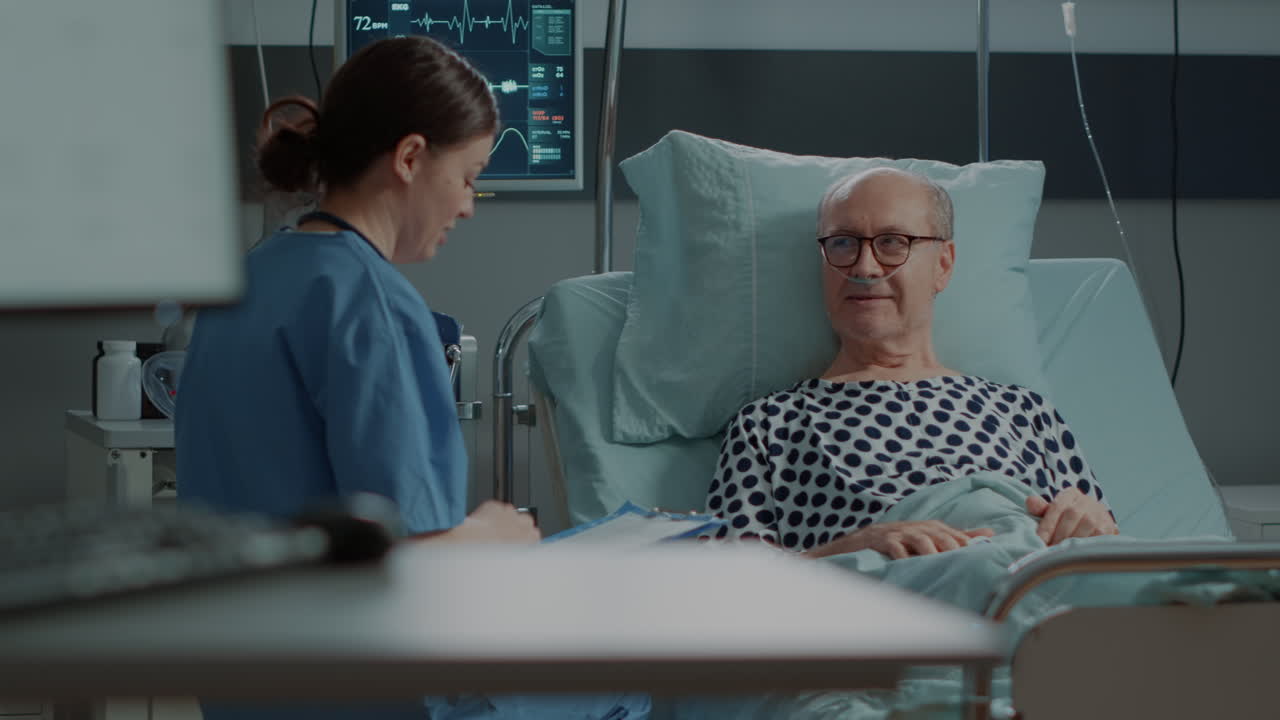 Nurse talking to sick old patient in hospital ward at unit