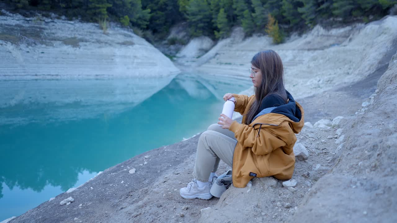 Woman enjoying a drink by a turquoise lake in nature