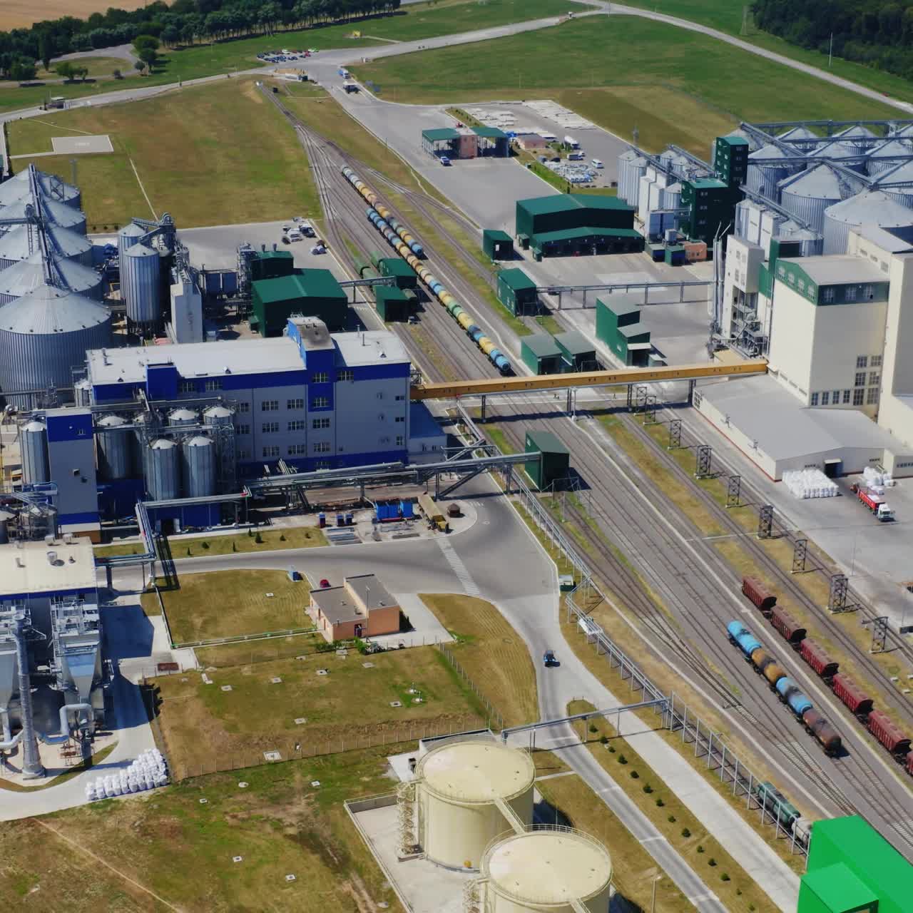 Agricultural plant with elevators. Large granary among nature. Industrial zone on field in summer. Steel grain silos. Aerial view.