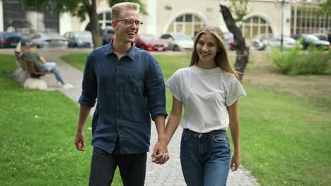 a young positive couple walks holding hands, meets in a summer city park. the girl and the boy are blonde. happy walk in the