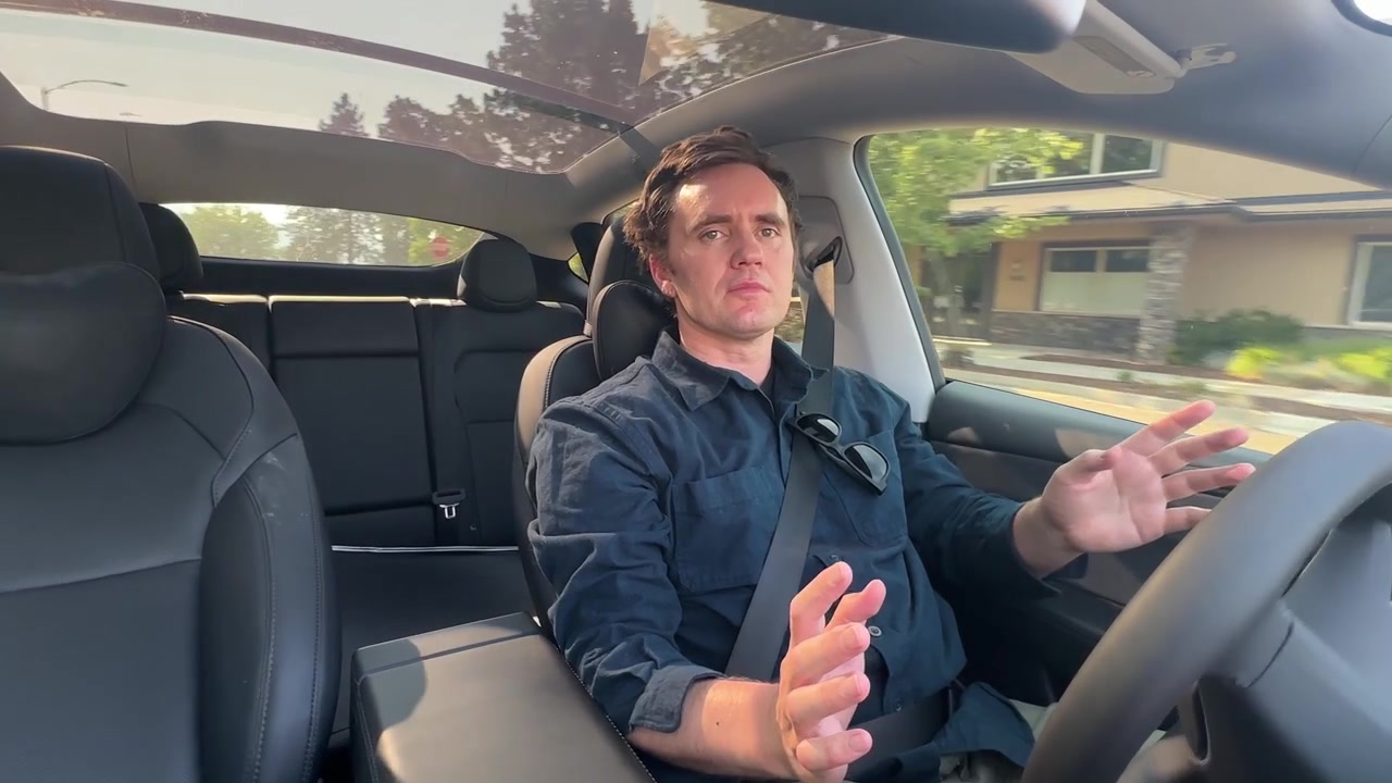 Man raises his hands off the wheel in mock surprise as his electric vehicle drives itself hands-free on autopilot.