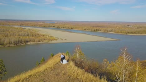 couple-stands-on-steep-river-bank-on-autumn-day-aerial-view
