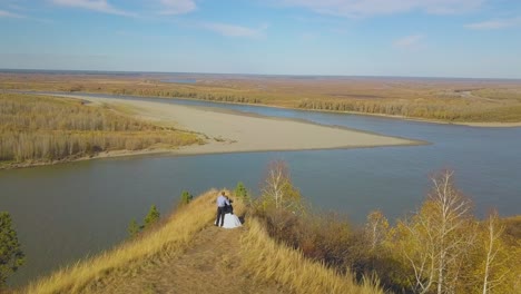 couple stands on steep river bank on autumn day aerial view