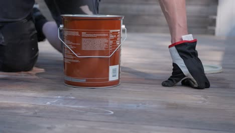 male hands with work gloves apply decking oil to a wood deck