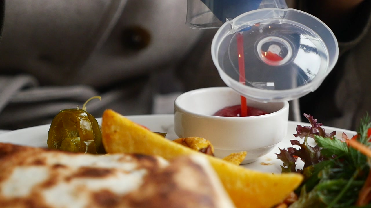 Pouring Ketchup into a Small Bowl on a Plate of Food