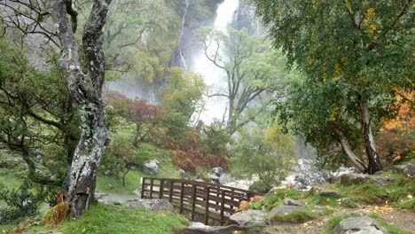 idyllic wooden bridge over valley waterfall cascading into powerful flowing river wide shot