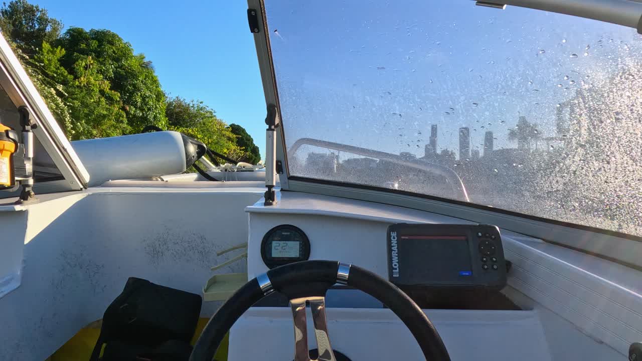 Point-of-view shot from inside an empty boat moving along a river, with city skyline ahead, bright daylight, and smooth camera motion