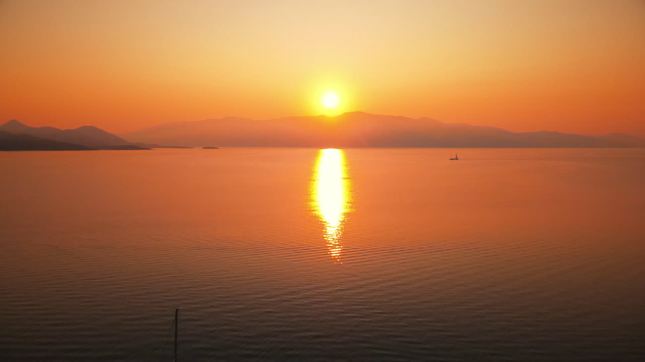 Sunset on the Ionian Sea coast, Greece. Bright Sun, land in the distance, floating boats, reflections in the water