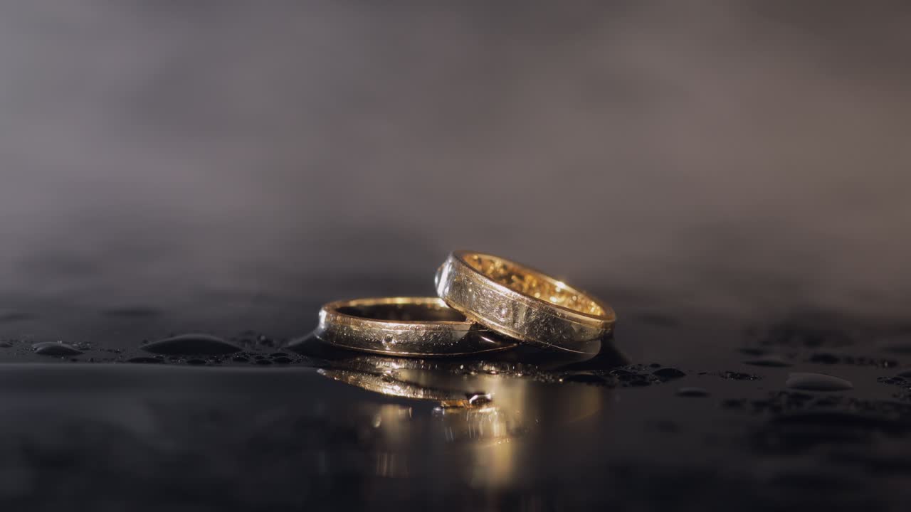 Wedding rings on dark water surface shining with light. Close up macro