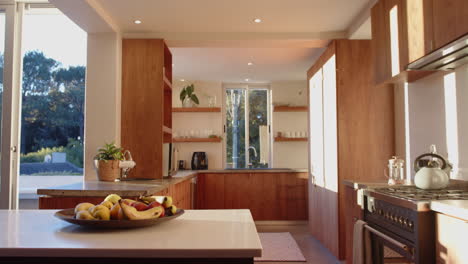 Modern kitchen with wooden cabinets and fruit bowl on countertop, sunlit interior, copy space