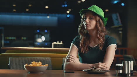 pretty young woman waiting for someone, worried, looking at the phone and wearing an irish green hat