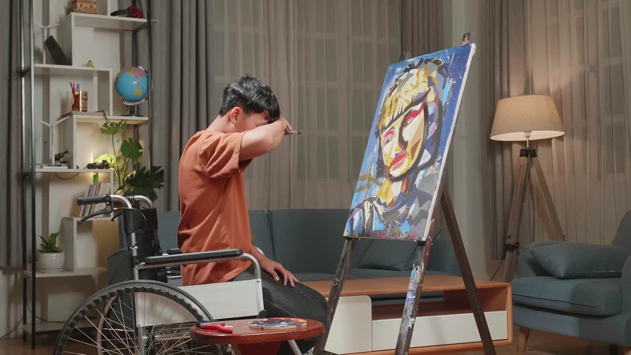 Side View An Asian Artist Boy In Wheelchair Holding Paintbrush Mixed Colour Turn To Cross His Arms And Smile While Painting A Girl On The Canvas