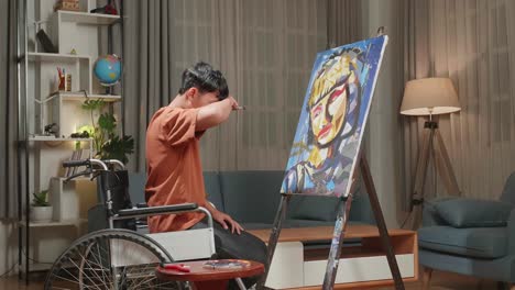 side view an asian artist boy in wheelchair holding paintbrush mixed colour turn to cross his arms and smile while painting a girl on the canvas