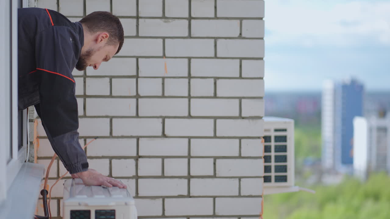 A male master at high altitude installs an air conditioner. Installation of the external unit of the Air Conditioning System. Summer air cooling