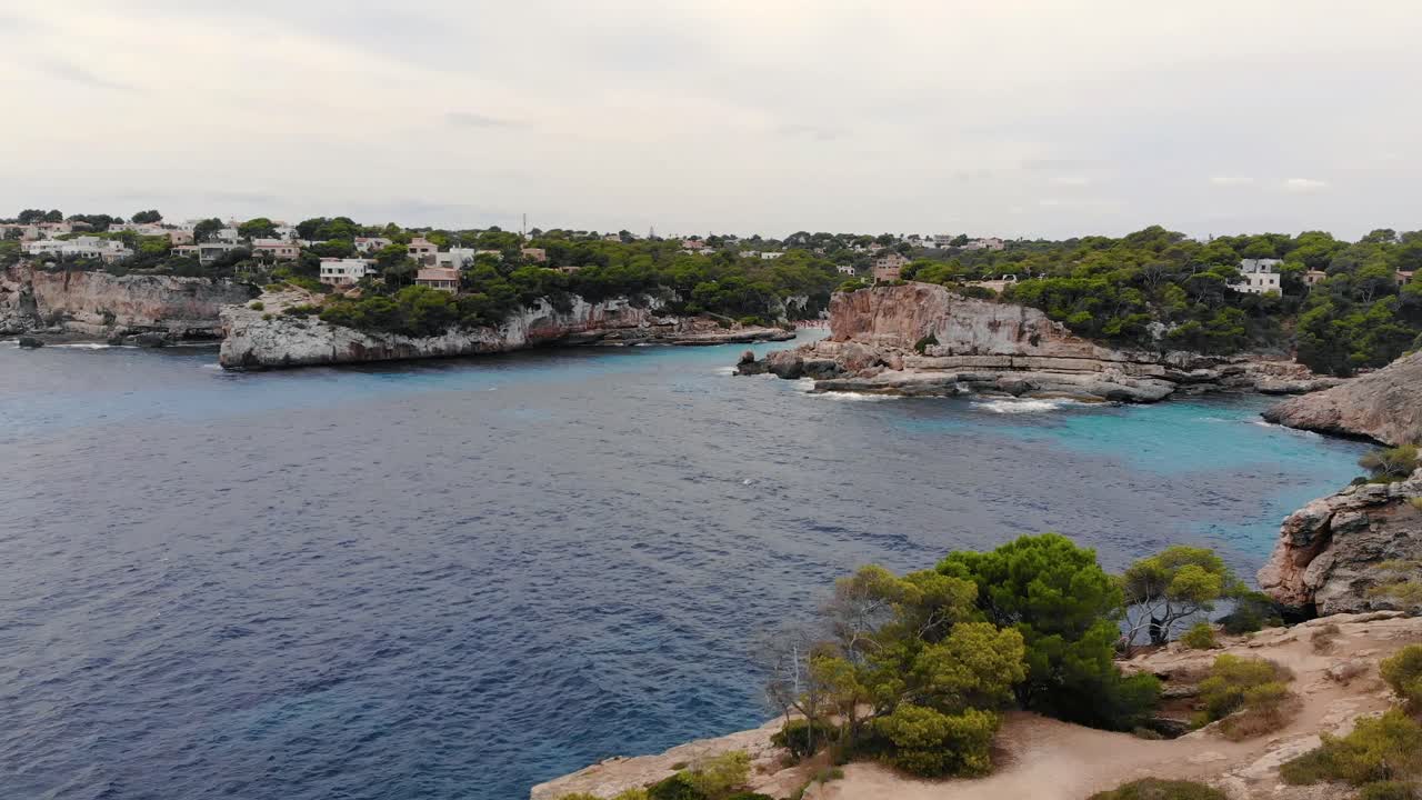 Ripresa aerea in movimento frontale sopra le acque cristalline e blu dell'isola di Maiorca, circondata da scogliere rocciose.