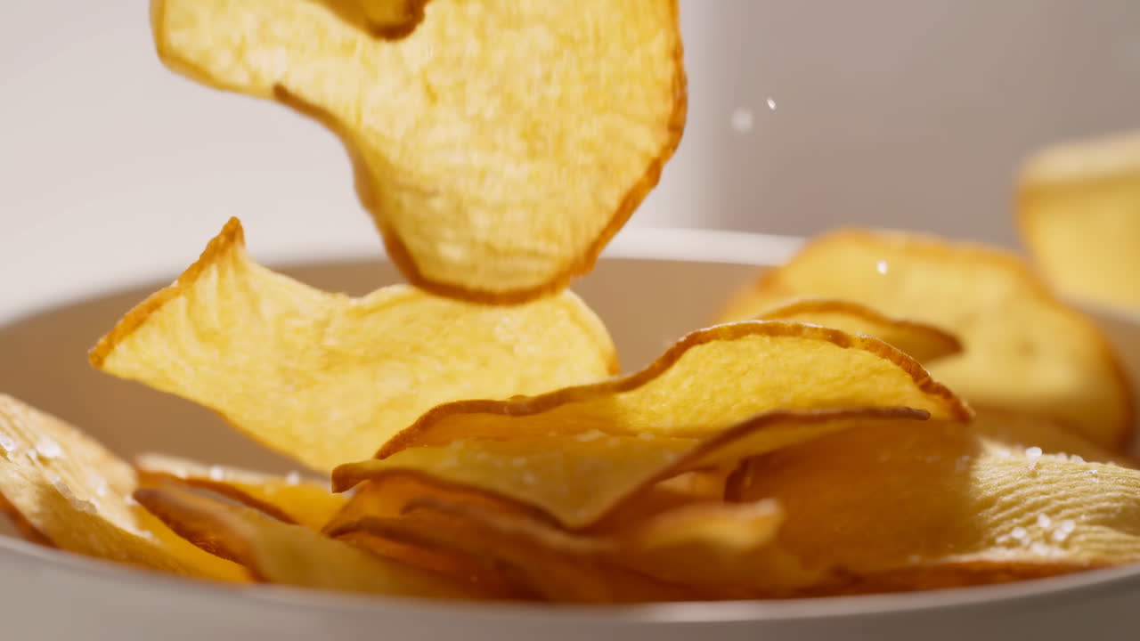 Crispy Potato Chips Falling Into Bowl, Golden Slices Catching Warm Studio Light, Visible Salt Crystals