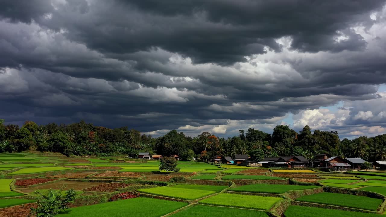 Lush green rice terraces creating a patchwork pattern under a dramatic cloudy sky, with traditional houses nestled among the fields, evoking a sense of tranquility and rural life in Southeast Asia
