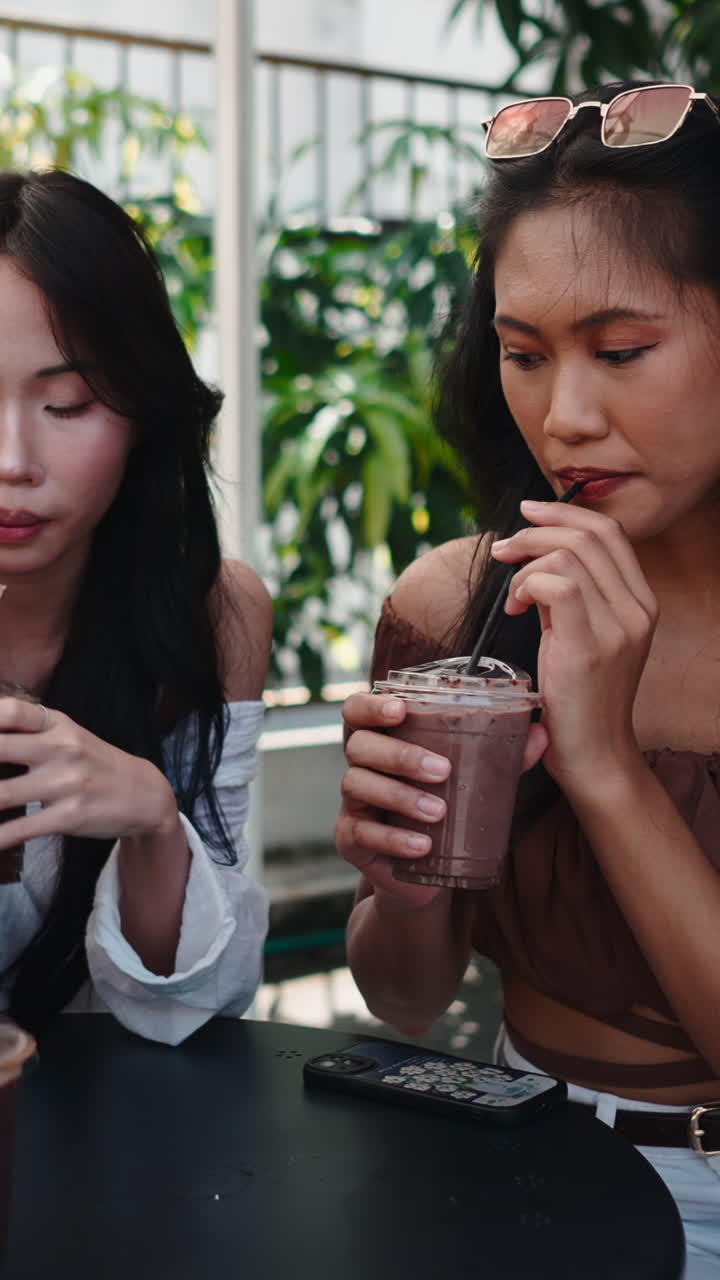 Những phụ nữ trẻ châu Á uống cà phê đá tại quán cà phê ngoài trời