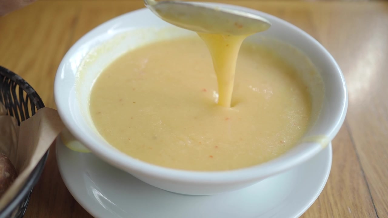 Person Stirring and Scooping Creamy Vegetable Soup in a White Bowl