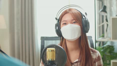 over shoulder view of man interview young female guest wearing protect mask and headphone for content in podcast studio. content creator concept