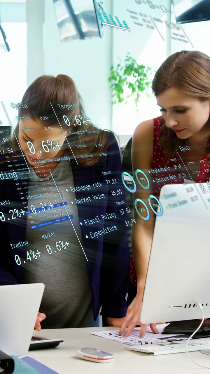 Vertikales Video: Zwei Frauen tippen auf Gerät und zeigen auf Monitor, HUD zeigt Diagramme für Finanzen.