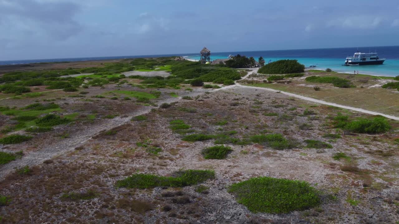 Aerial over flat Caribbean beach with roof palapas and boat in water