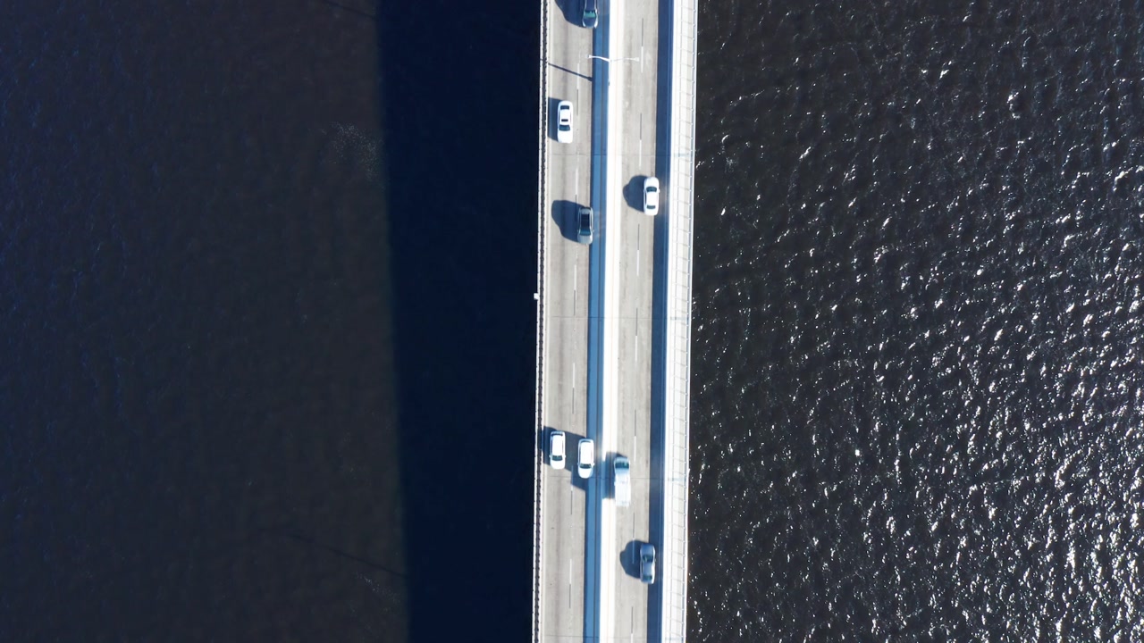 Cars travel across a bridge spanning dark waters, casting shadows below. Ideal for traffic, infrastructure, and urban planning projects.