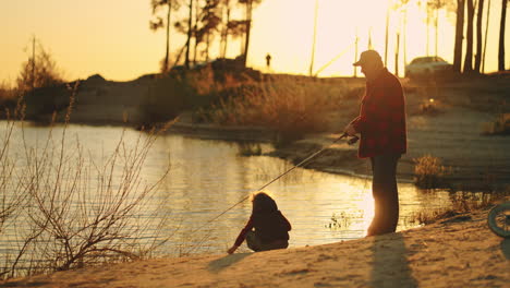 Un-Viejo-Pescador-Y-Un-Niño-Pequeño-Pasan-Tiempo-En-La-Orilla-Del-Lago-O-Del-Río-Pescando-En-Familia-Al-Atardecer