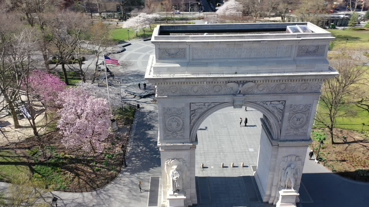 An aerial, day time view of the Washington Square Arch. The drone orbits the arch, counterclockwise with an empty Washington Square Park in the background.