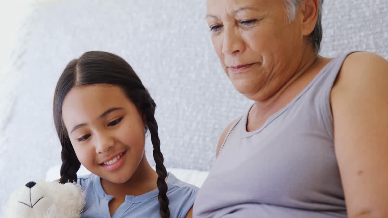 할머니와 손녀가 침실 4k에서 함께 사진 앨범을 보고 있습니다.