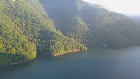 Morning-golden-hour-light-o-forest-and-hills-beside-peaceful-Lake-Tarnita,-Romania