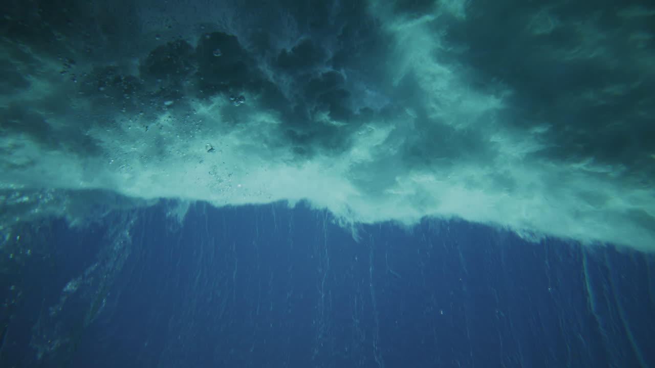 Sun rays view from underwater as ocean wave crashes and swirls in slow motion, mesmerizing pattern