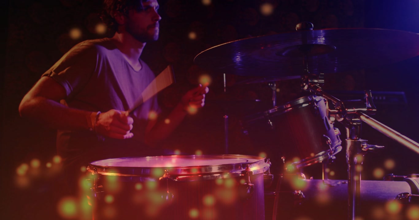 Male drummer playing snare toms cymbals in dim stage camera panning sparking bokeh accenting music