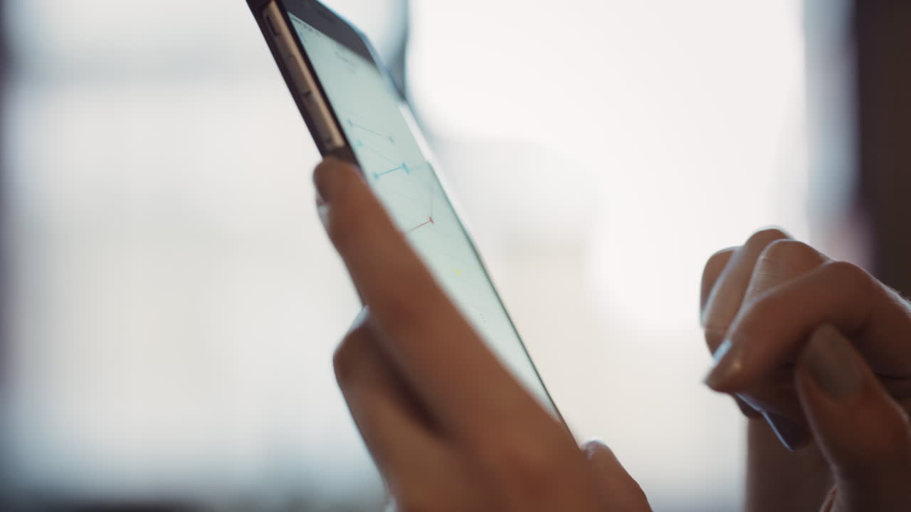 cerca de las manos de las mujeres usando el teléfono inteligente para leer gráficos de negocios