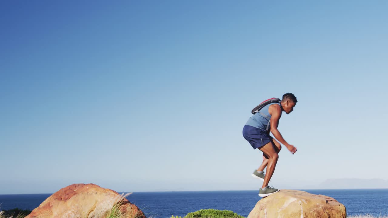 African american man exercising outdoors jumping on rocks in countryside on a mountain