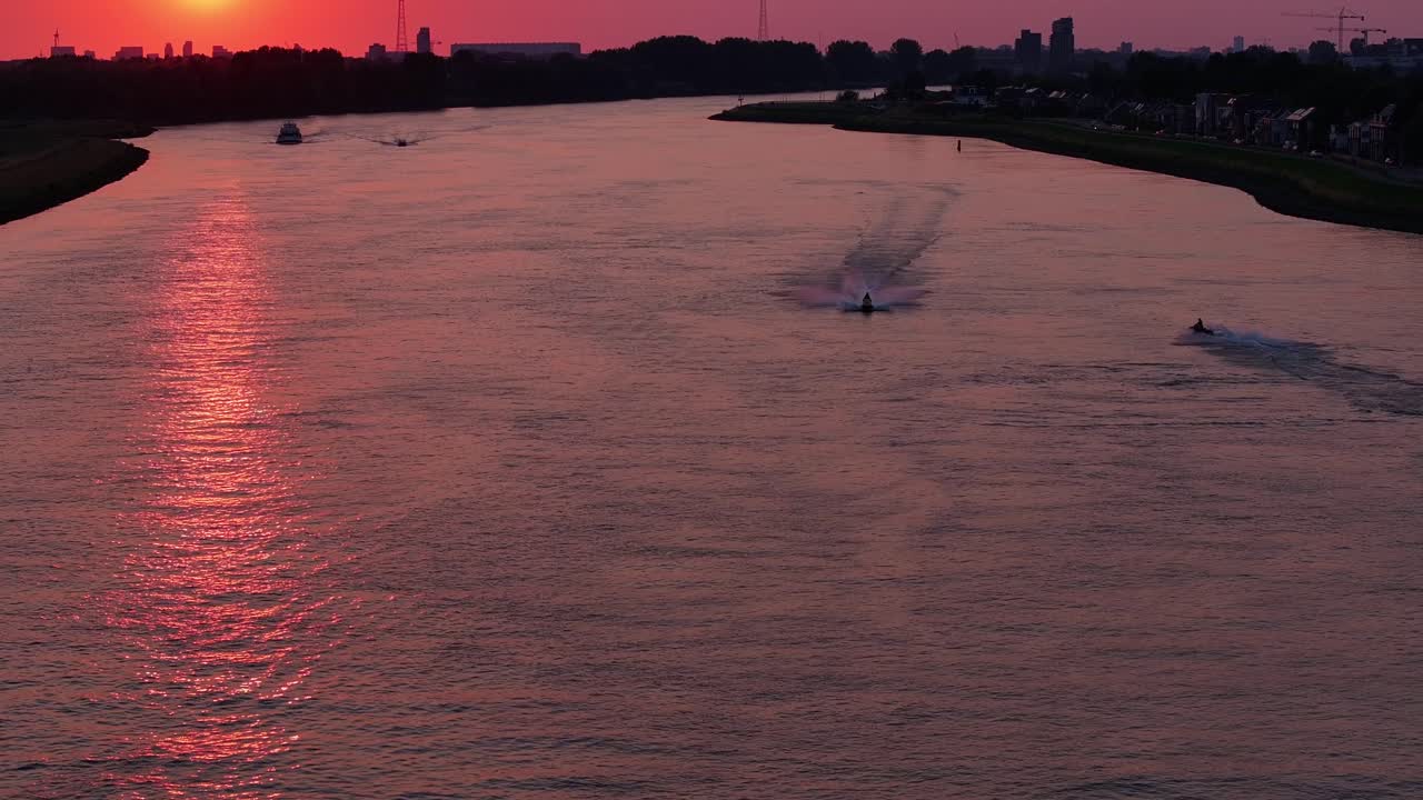 pilotos de jet-ski acelerando a lo largo de un río bajo la puesta de sol roja de una noche de rotterdam