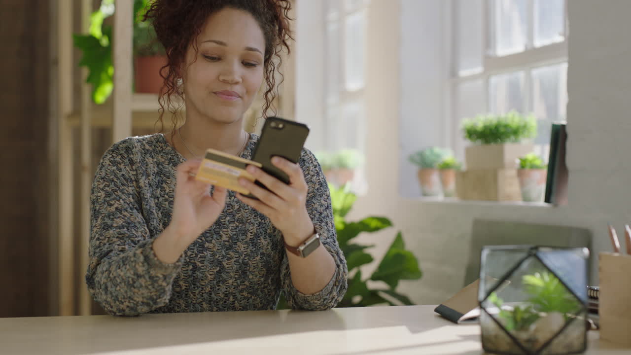 joven mujer de raza mixta comprando en línea usando una aplicación de comercio electrónico de teléfono inteligente sonriendo disfrutando de la compra en línea en un apartamento de loft sostenible