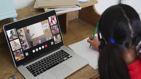 Girl-doing-homework-and-having-a-video-conference-with-teacher-and-classmates-on-laptop-at-home