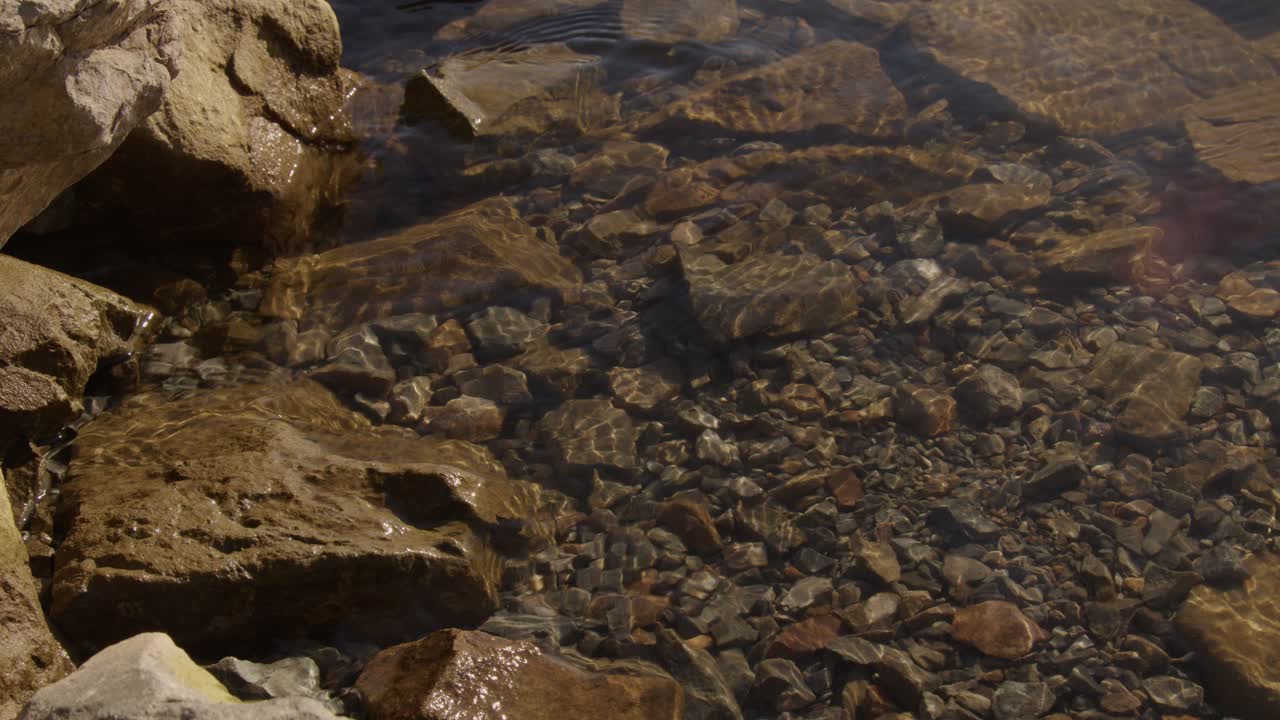Close-up shot of clear water gently hitting and splashing against rocks on the shore