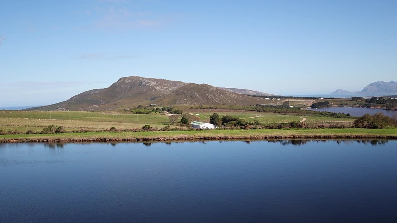 Panorámica aérea sobre un lago azul en el exuberante valle verde de Hemel-en-Aarde