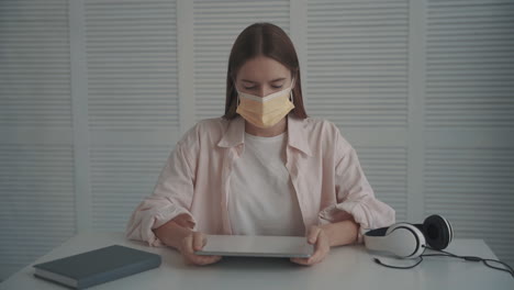 mujer joven con mascarilla sosteniendo una tableta tiene una videollamada