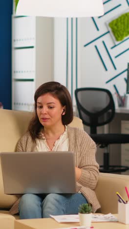vertical video business woman talking during video conference calling from laptop sitting on couch