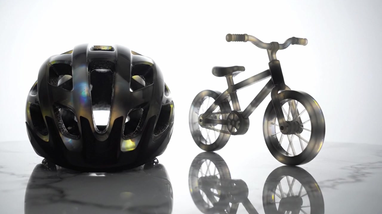 A close-up view of a glossy bicycle helmet and a sleek bicycle model presented on a marble surface, emphasizing their design and craftsmanship in stark lighting.