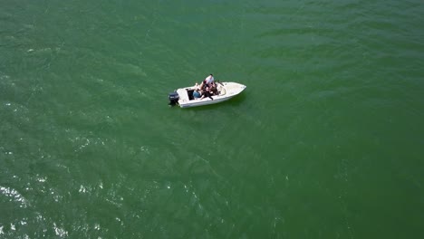 aerial slow upwards pan of people in white motor boat on lake in valley with trees and blue skies in the background