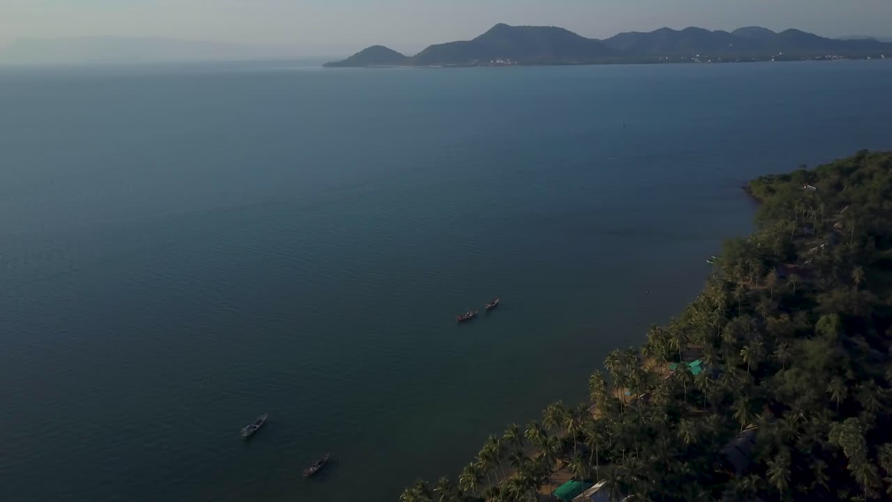 Aerial view of a tropical island coast with boats and mountains