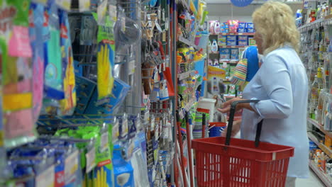 una mujer mayor está eligiendo artículos para el hogar en el supermercado con una canasta de la tienda para la limpieza
