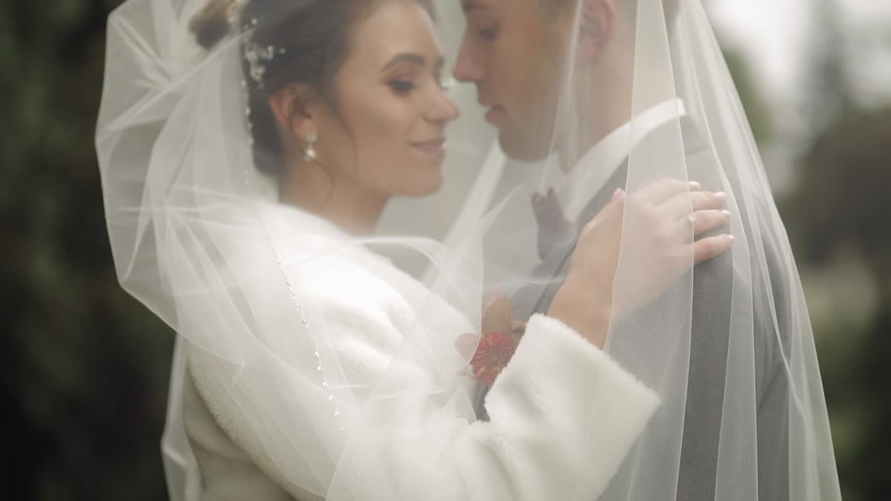 Adorabili novelli sposi caucasici, la sposa che abbraccia lo sposo nel parco mentre si baciano, coppia di sposi che si abbraccia