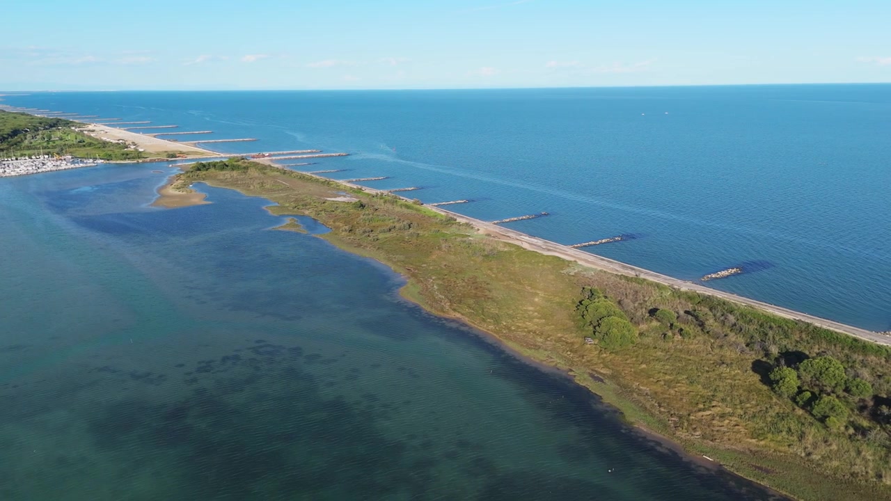 Luftfoto dronepanorama som sporer den tynne sandhalvøya som skiller grønne lagunesaltmyrer fra rolige, åpne havområder ved solnedgang nær Eraclea og Piave-elvemunningen, Italia